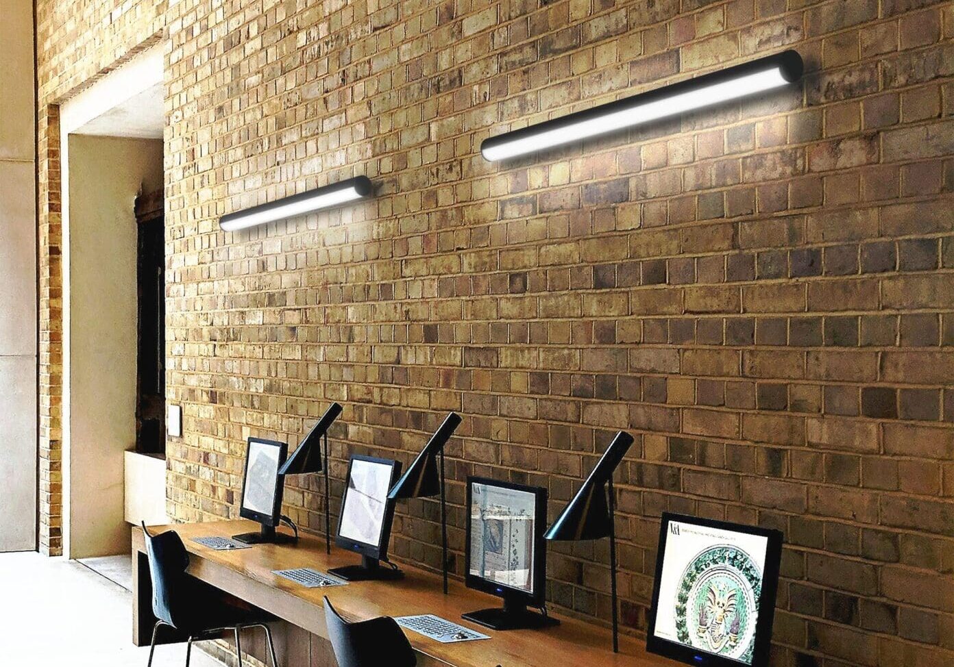 Modern workspace with computers against a brick wall and sleek lighting.
